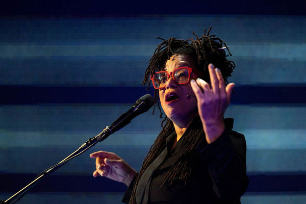 Pamela Z standing at a microphone with her hand in the air