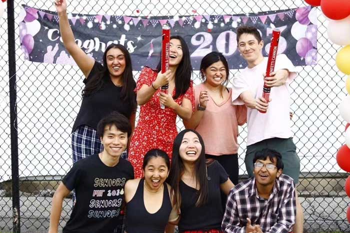8 excited 2023 class council members shoot off confetti cannons while wearing flannel pants outside under a balloon arch